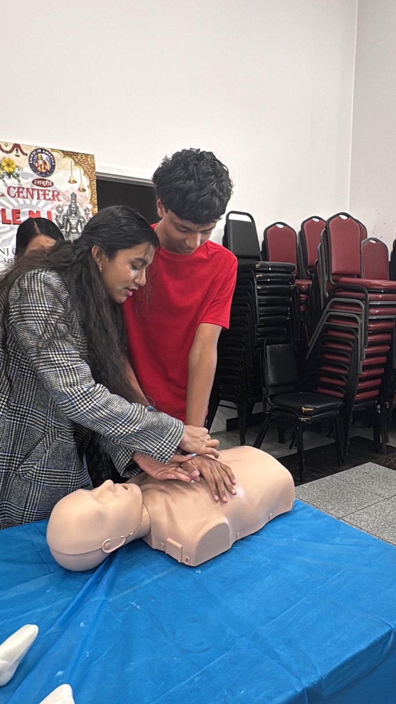 Sharanya guiding a student's hands through chest compressions on a CPR mannequin